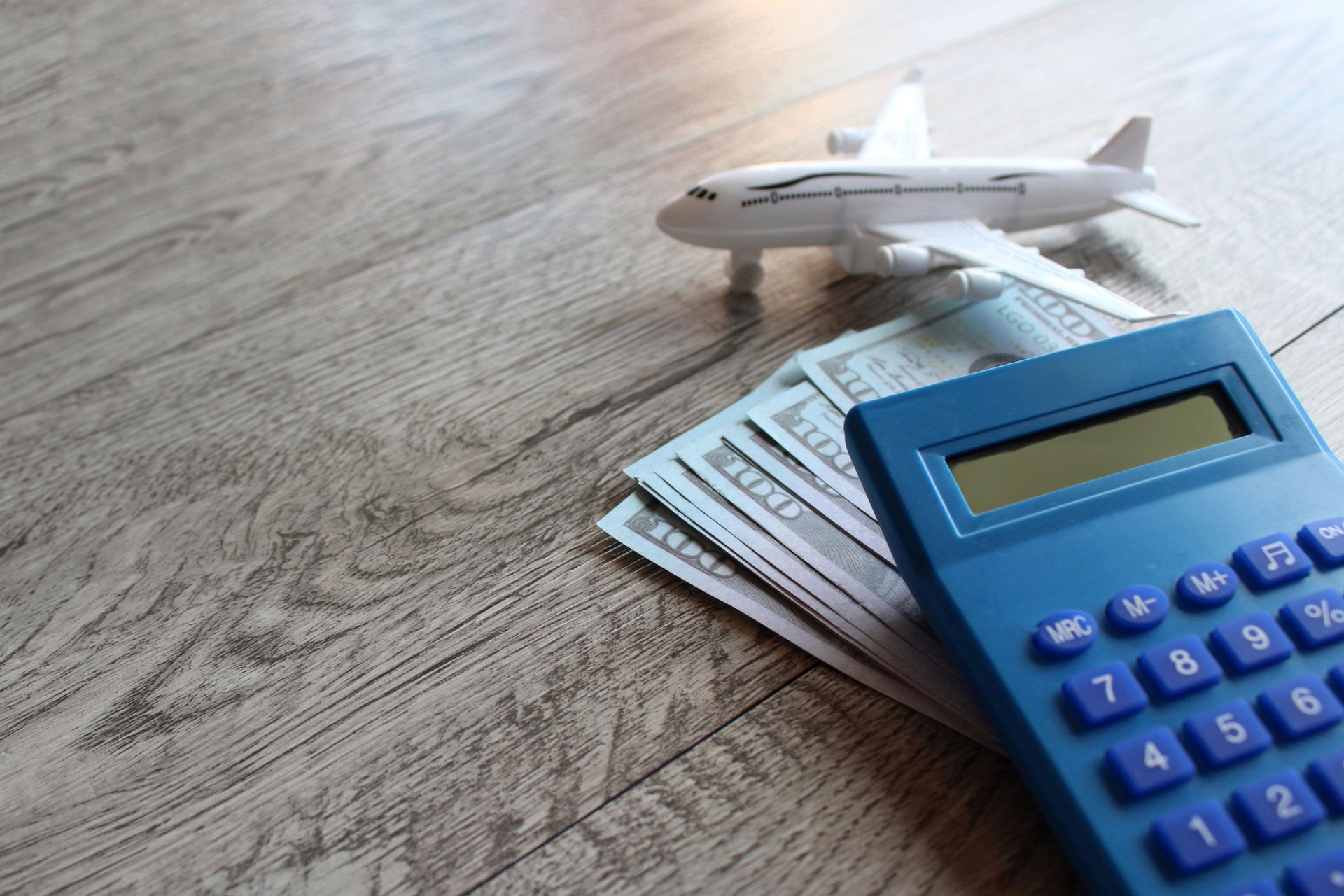 Toy plane, money and calculator on wooden table with copy space